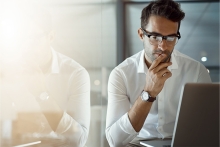 Business man wearing white dress shirt, watch, and glasses working on computer