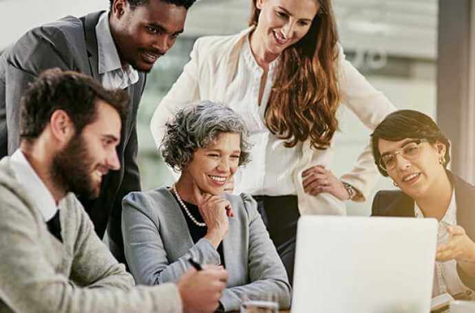 men and women gathered around a laptop and smiling