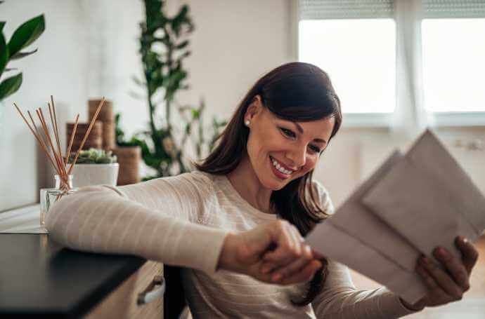 a brunette smiling woman opening letters in her living room