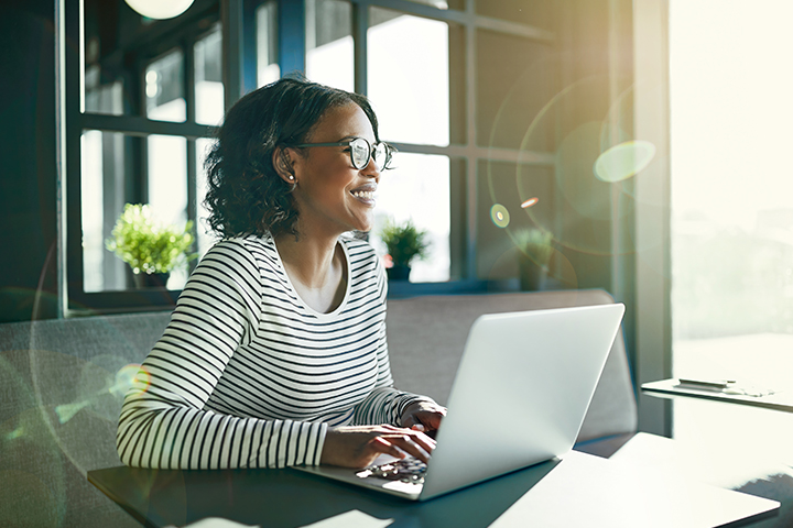 smiling woman using laptop in sunny office smiling woman using laptop in sunny office