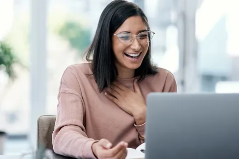 a happy brunette woman wearing glasses smiling at her laptop