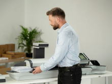 Man standing at an office table using a postage meter to process mail in a modern workspace.